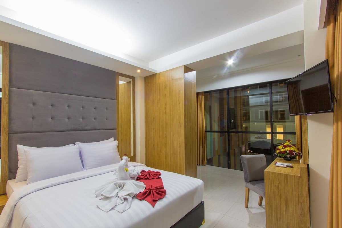 Une chambre d’hôtel moderne dotée d’un grand lit, d’une tête de lit en bois, d’un téléviseur à écran plat et d’un petit bureau agrémenté d’un vase de fleurs.