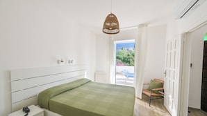 A bedroom with a bed, bedside table, and a wicker pendant light. - Residence San Domenico (Forio)