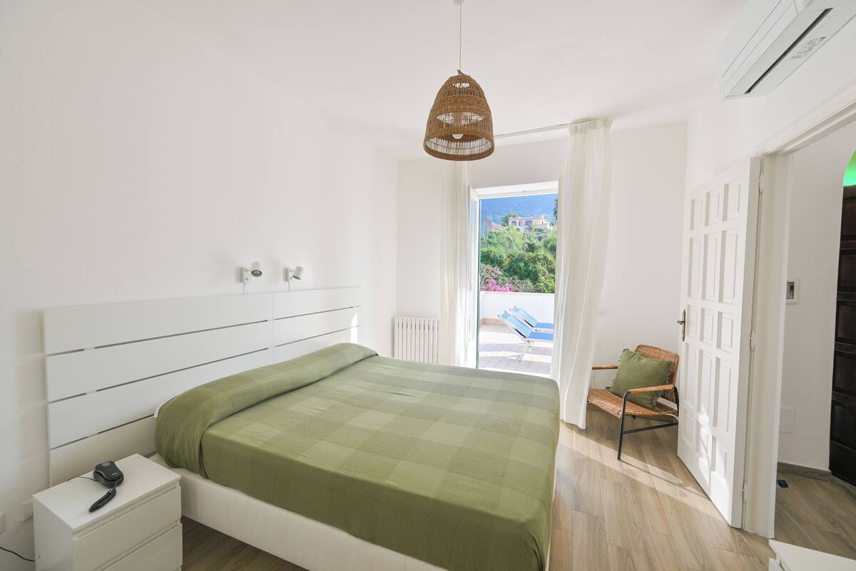 Un dormitorio con cama, mesita de noche y una lámpara colgante de mimbre.