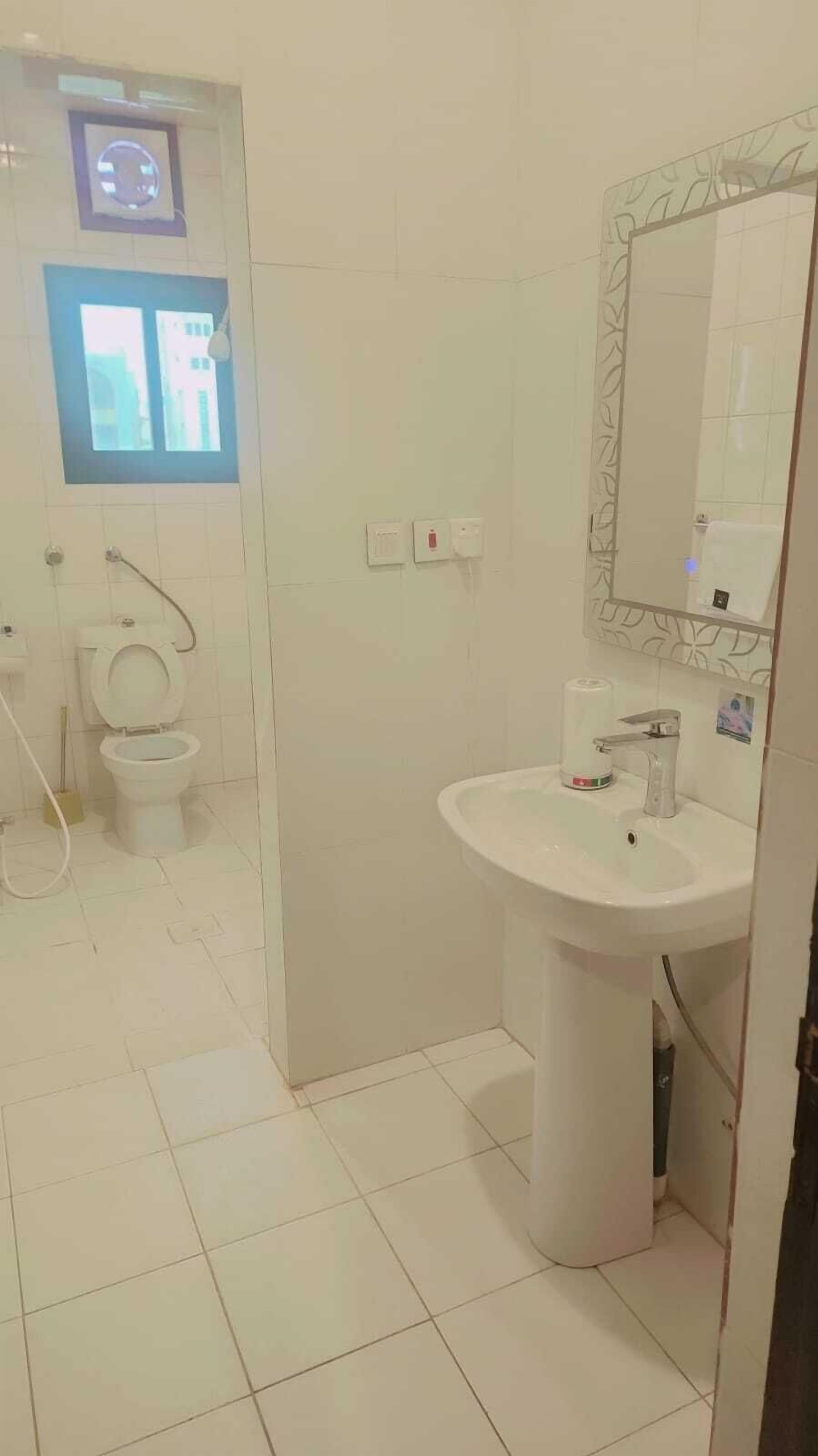 Un bagno con il water, un lavandino e uno specchio. Si vede una finestra sopra il water e un lampadario fissato al muro.