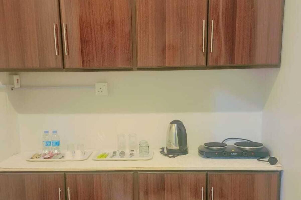 A kitchen with wooden cabinets, a countertop with a kettle, cups, and a coffee maker.