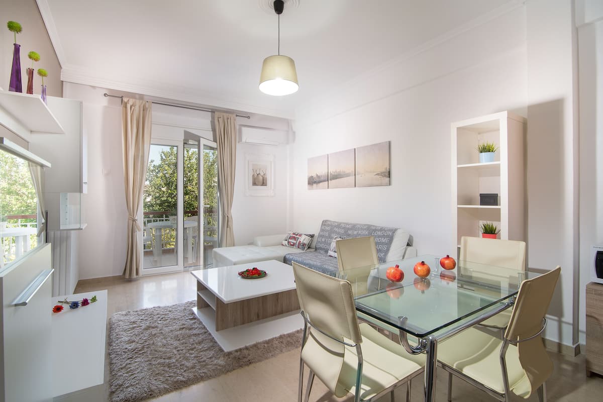 Una sala de estar moderna con una mesa de comedor de vidrio, sillas color beige, un sofá blanco y una mesa de centro de vidrio.