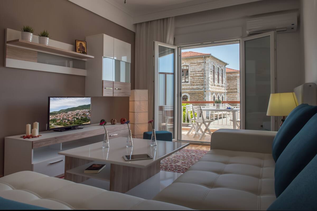 Una sala de estar moderna con sofá, televisión y balcón con vista a un edificio histórico.