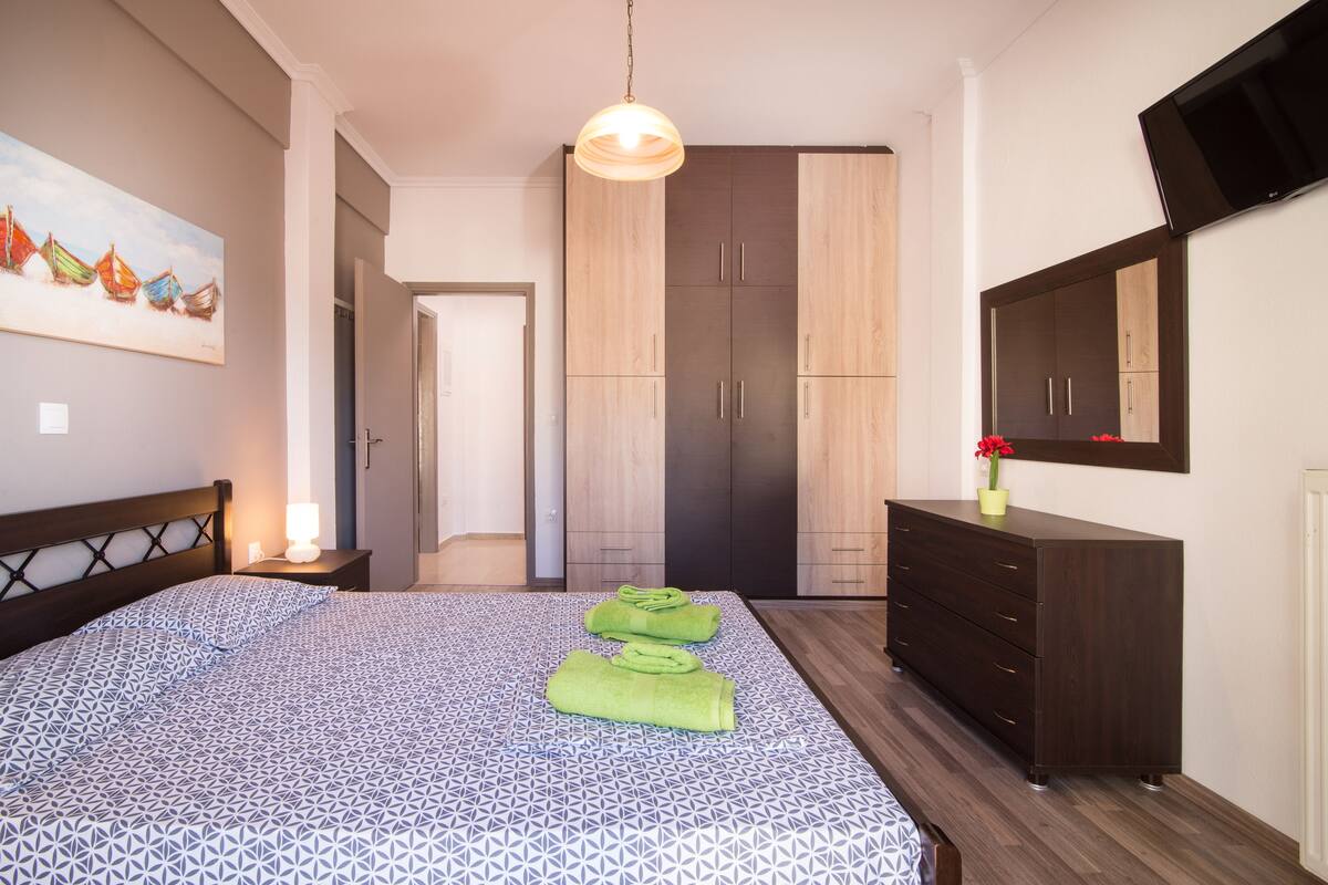 Un dormitorio con cama, mesita de noche, cómoda, espejo y un cuadro en la pared.