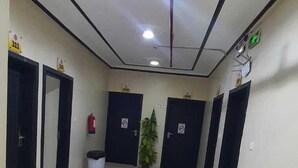 A hallway with multiple doors, each marked with a number. There is a trash bin and a potted plant in the center. - Al Eairy Serviced Apartments Company  (Buraydah)