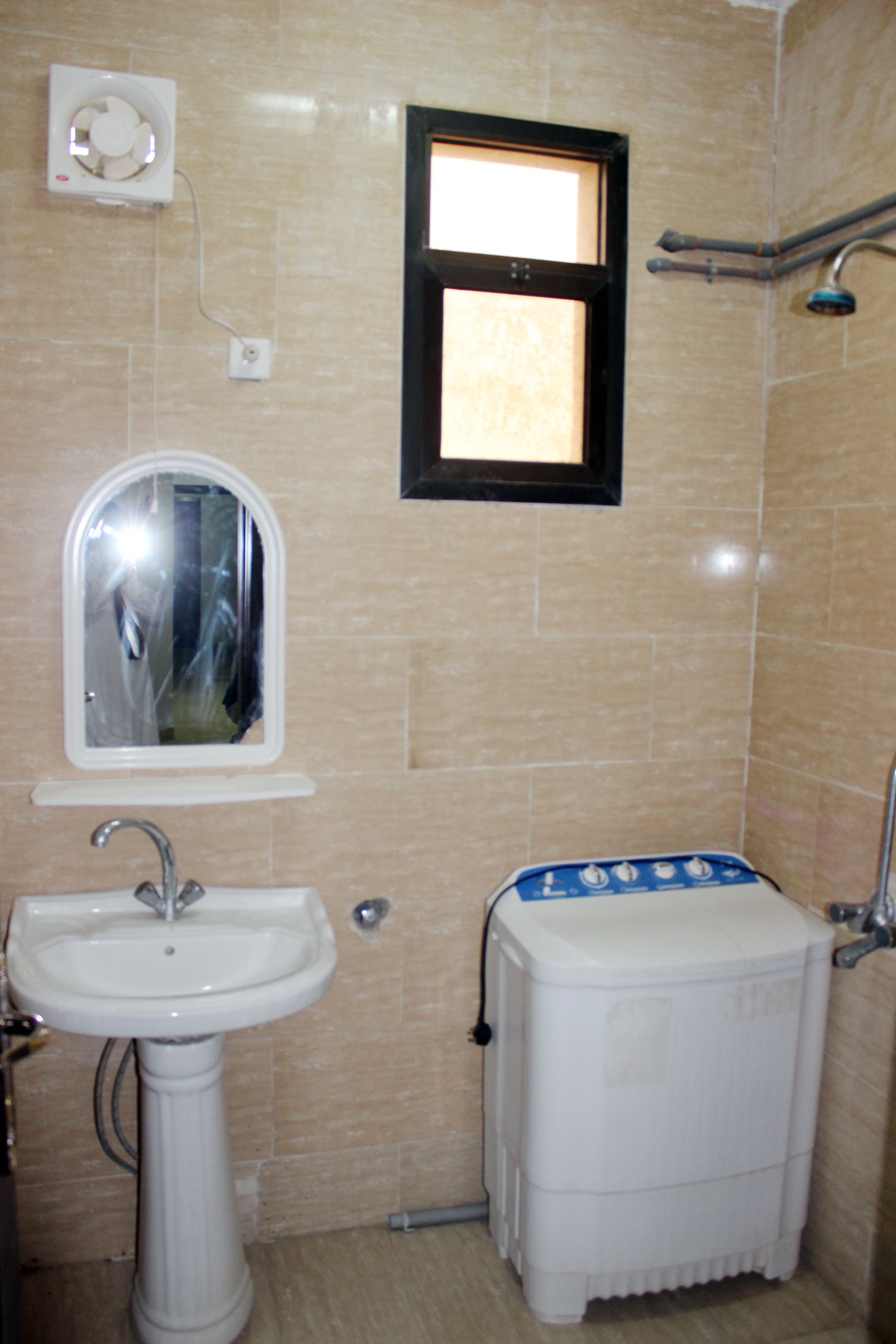 Un baño con lavamanos pedestal, espejo, ventana y retrete con tanque de agua.