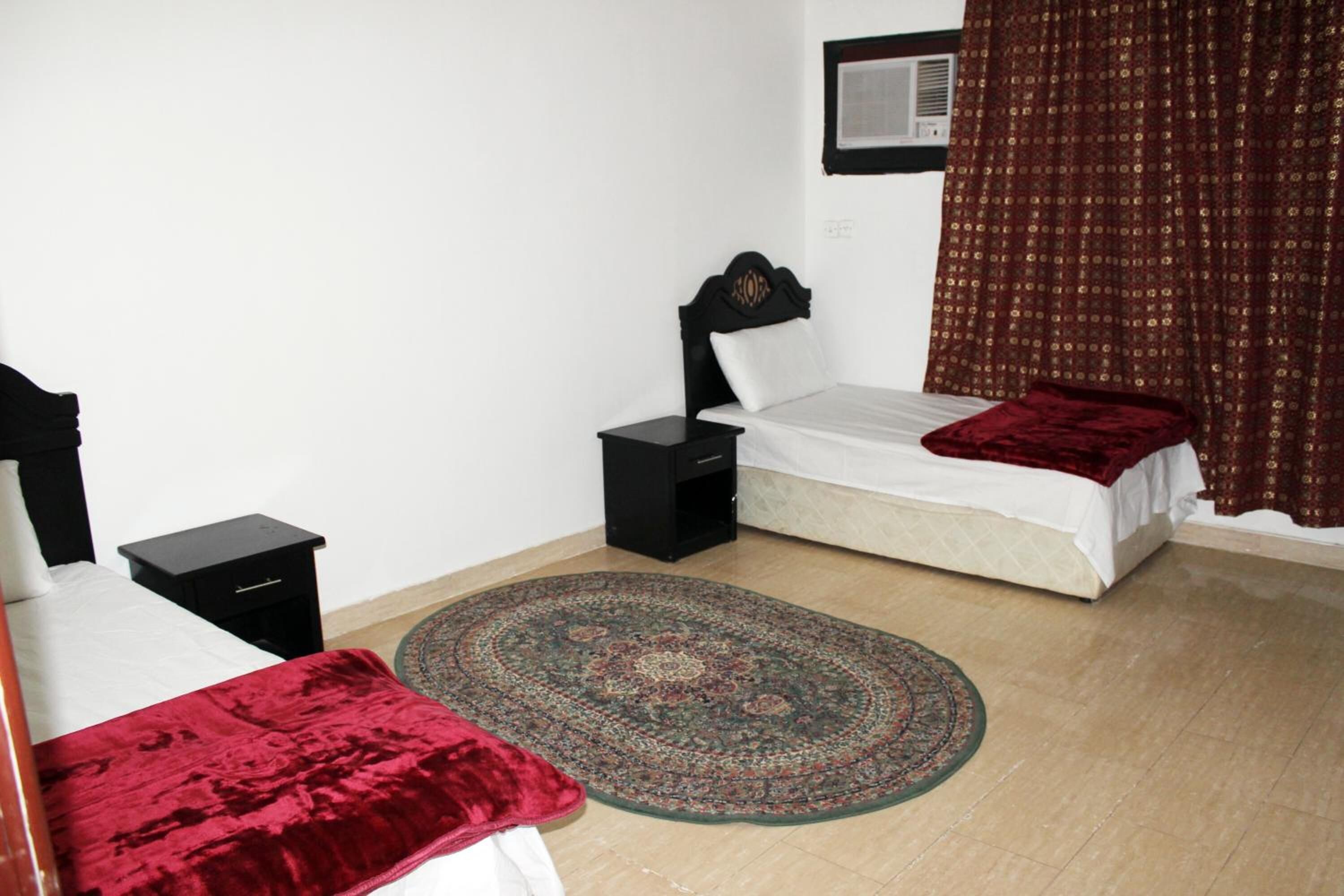 A bedroom with two beds, a large rug, and a window with curtains.