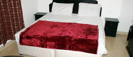 A neatly made bed with a red blanket, white pillows, and a black headboard. There are two bedside tables, one on each side of the bed.