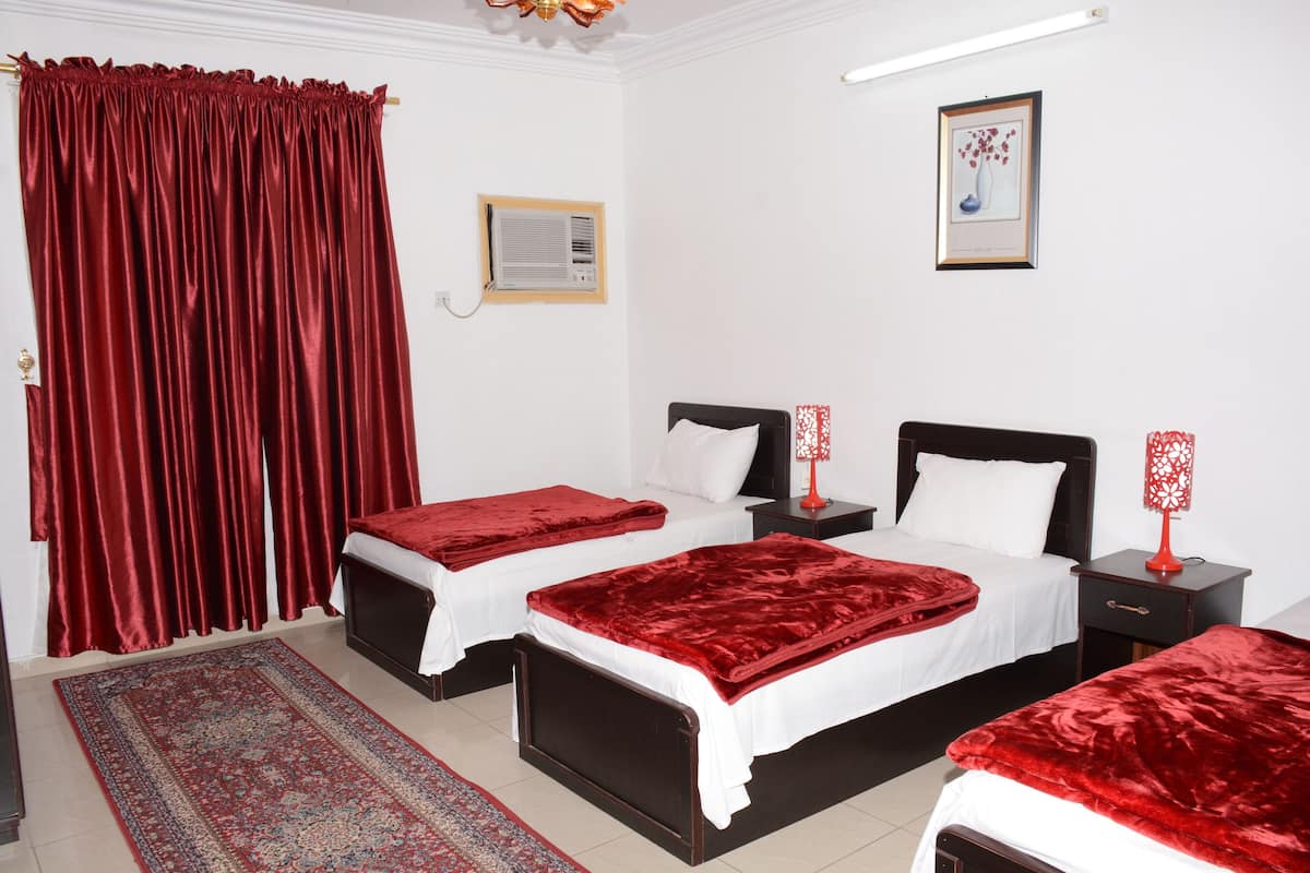 Habitación de hotel con dos camas, ropa de cama roja, alfombra estampada, cortina roja, un cuadro en la pared y una lámpara roja en la mesita de noche.