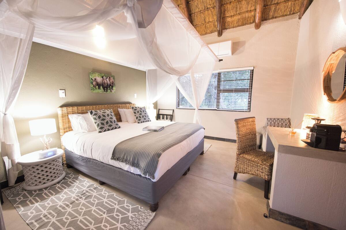A bedroom with a bed, bedside table, chair, and a small desk with a lamp.
