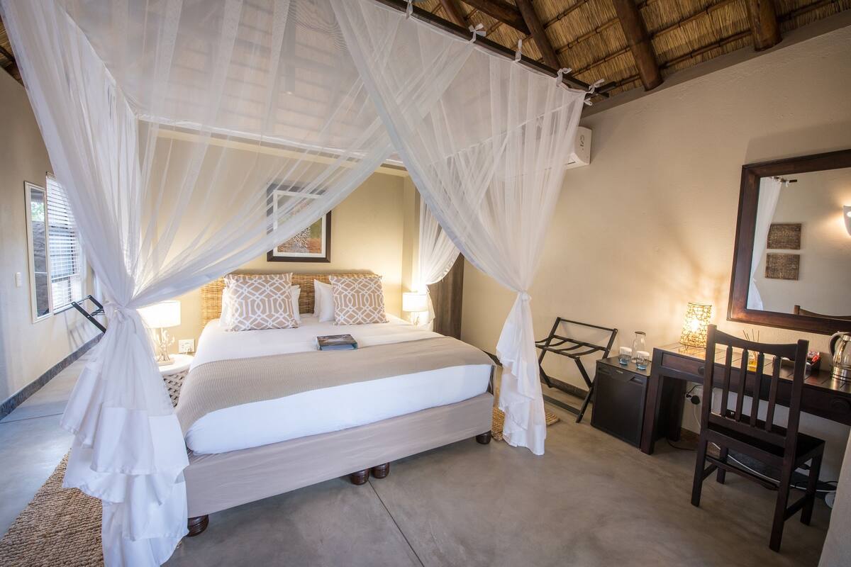 A bedroom with a bed, bedside table, chair, and a desk with a lamp.