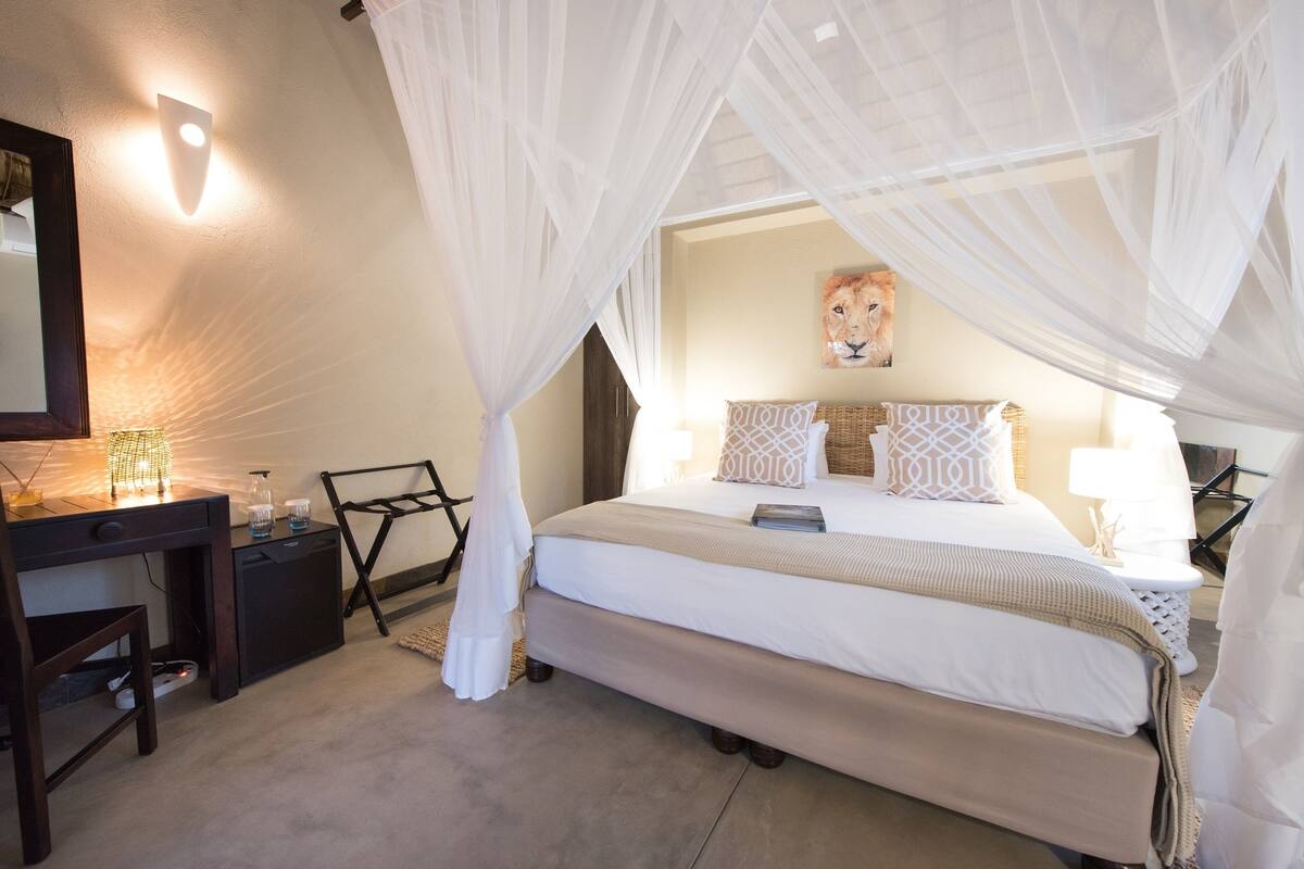 A bedroom with a bed, bedside tables, a desk, a chair, a lamp, and a painting on the wall.