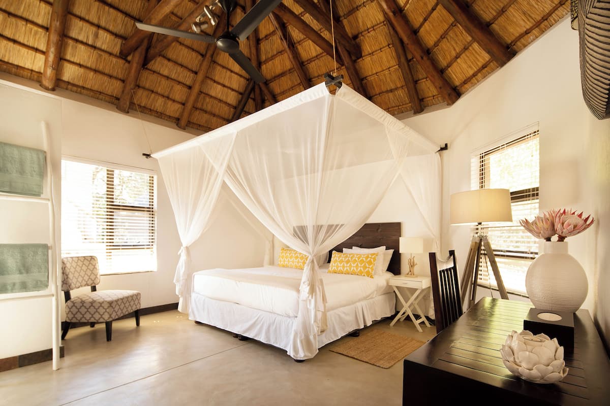 A bedroom with a four-poster bed, a chair, a desk, and a lamp.