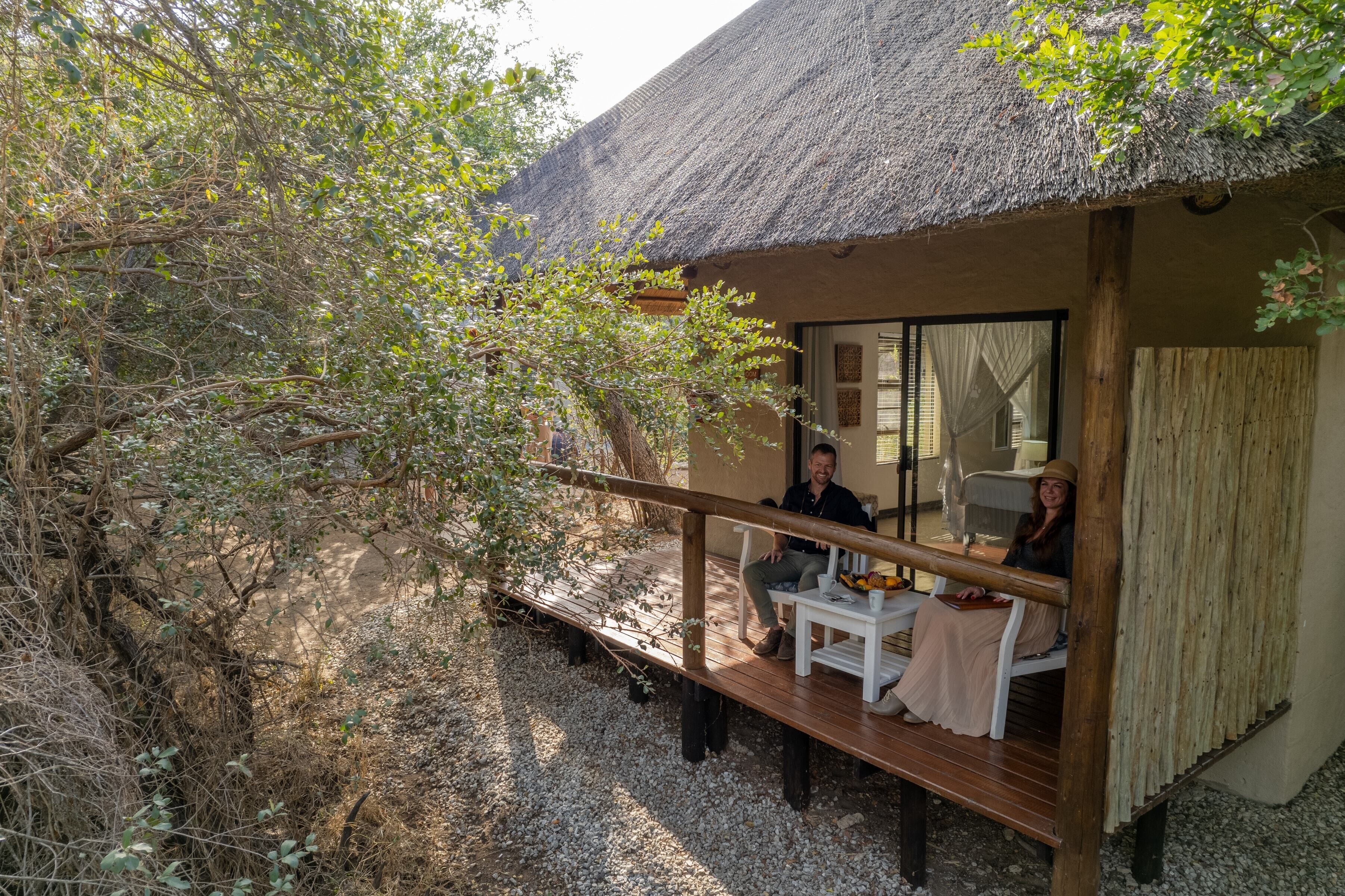 A thatched-roof structure with a wooden deck and a glass door leading inside.