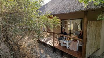 A thatched-roof structure with a wooden deck and a glass door leading inside.