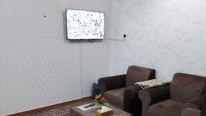Un salon comprenant un canapé marron, une table basse, un tapis à motifs et un téléviseur à écran plat fixé au mur.