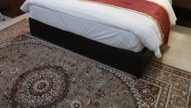 Une chambre à coucher avec un grand lit, une tête de lit en bois, des tables de chevet et un tapis à motifs.