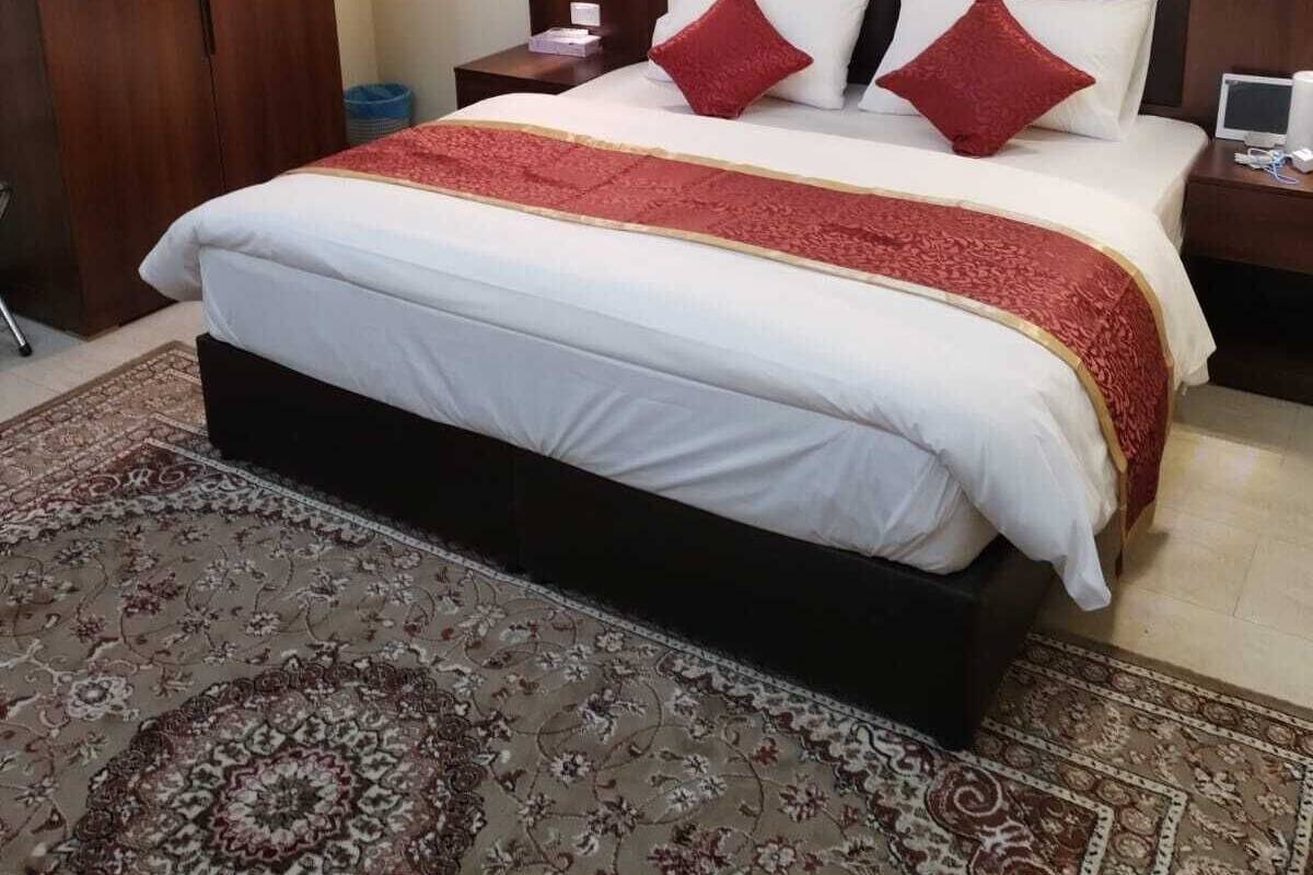 Ein Schlafzimmer mit einem großen Bett, einem Holz-Kopfteil, Nachttischen und einem gemusterten Teppich.