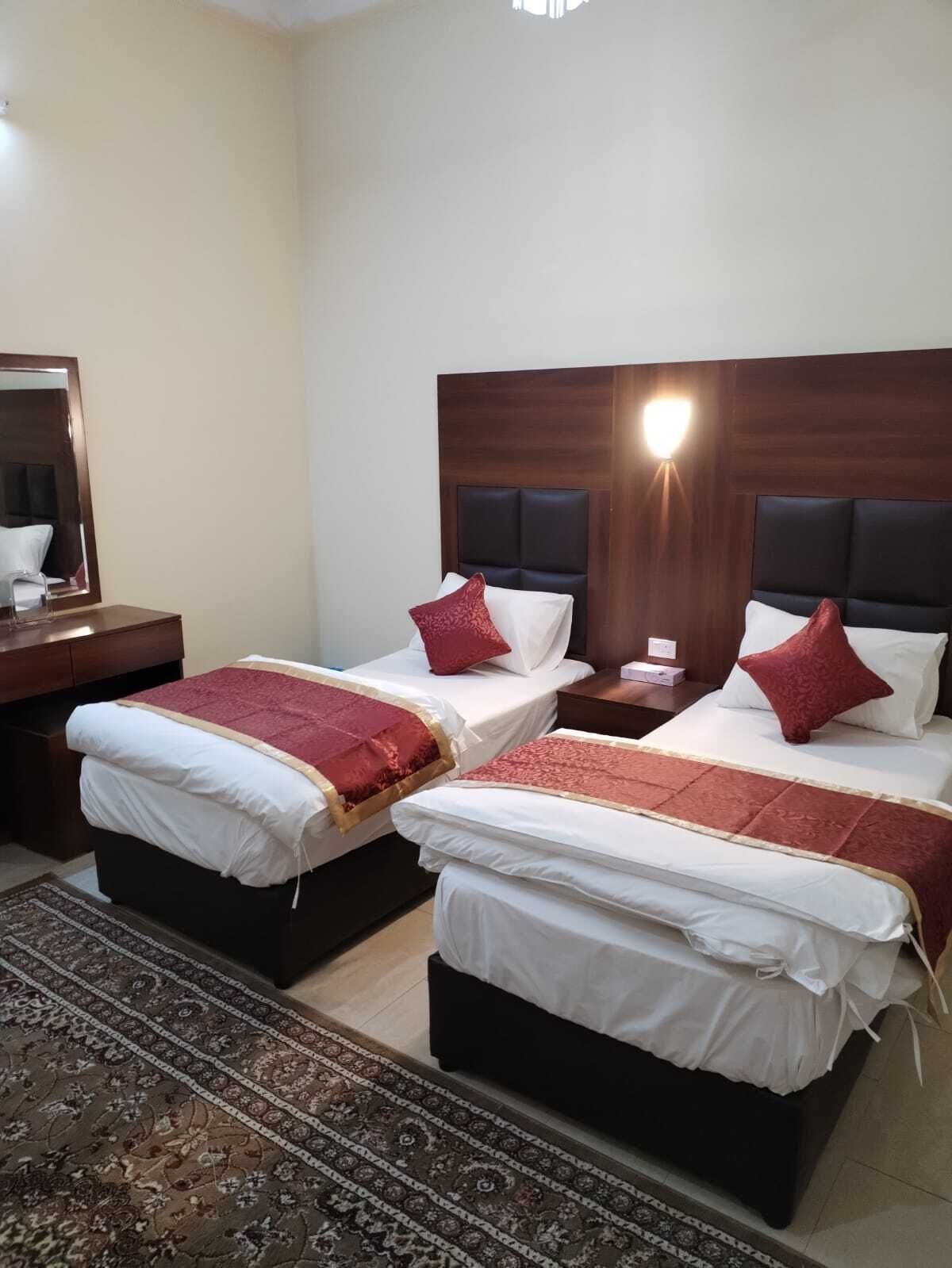 Una habitació d'hotel amb dos llits, cadascun amb capçalera, taula de nit i falda de llit.