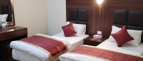 A hotel room with two beds, each with a headboard, a bedside table, and a nightstand.