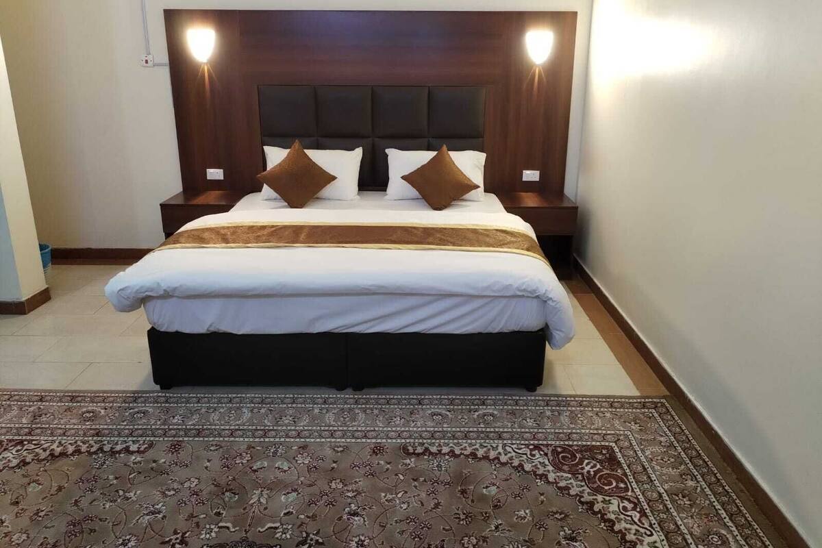 Ein ordentlich bezogenes Bett mit Kopfteil, zwei Nachttischen und einem gemusterten Teppich.
