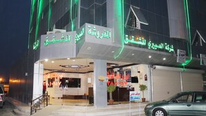 A hotel entrance with Arabic signage, a visible reception desk, and a parked car.