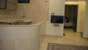 A modern kitchen with a built-in island, a flat-screen TV mounted on the wall, and a doorway leading to a bedroom.