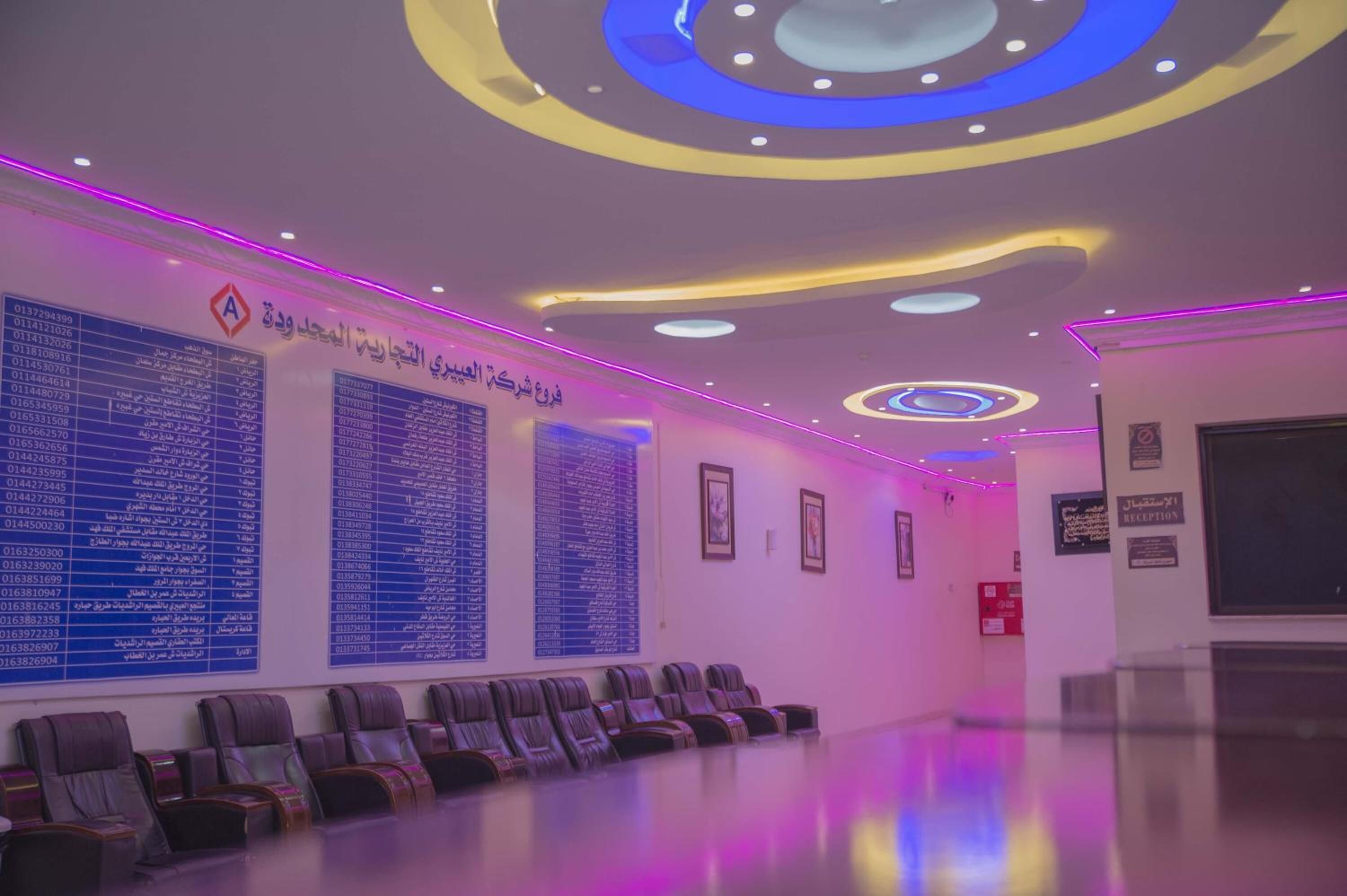Une salle d’attente moderne, avec des rangées de chaises, un comptoir d’accueil et des panneaux d’information fixés aux murs.
