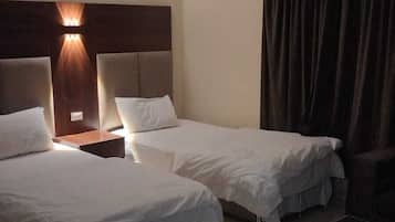 Habitación de hotel con dos camas, una mesita de noche, una lámpara, una cortina y una pequeña mesa.
