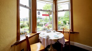 Un rincón comedor con una mesa lista para dos personas, una silla y vistas a un jardín a través de amplias ventanas.