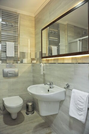 A modern bathroom with a toilet, bidet, sink, and a large mirror.