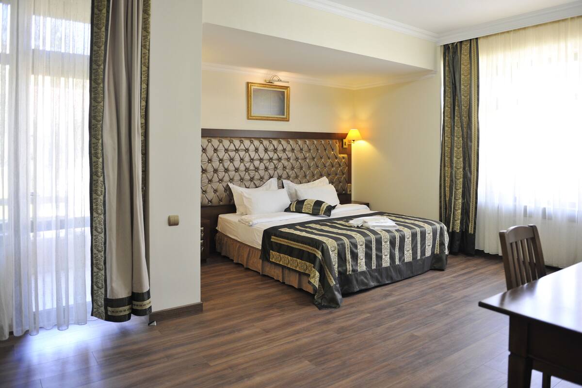 A hotel room with a large bed, a wooden headboard, a bedside table, and a chair.