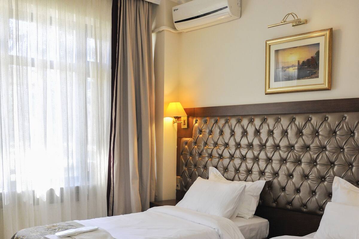 A hotel room with two beds, a large tufted headboard, a framed picture on the wall, and an air conditioning unit.
