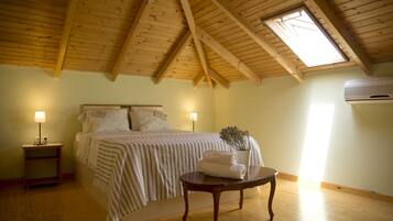 A bedroom with a sloped wooden ceiling, a bed with a striped bedspread, two bedside lamps, a bedside table with a folded towel, and an air conditioning unit on the wall.