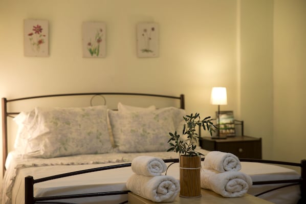 A neatly made bed with rolled towels and a potted plant on a bedside table.