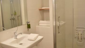 Une salle de bain moderne avec une douche à parois de verre, un lavabo blanc avec un miroir au-dessus et une étagère avec des serviettes.