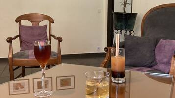 A living room with a glass table, two chairs, a sofa, and a potted plant.