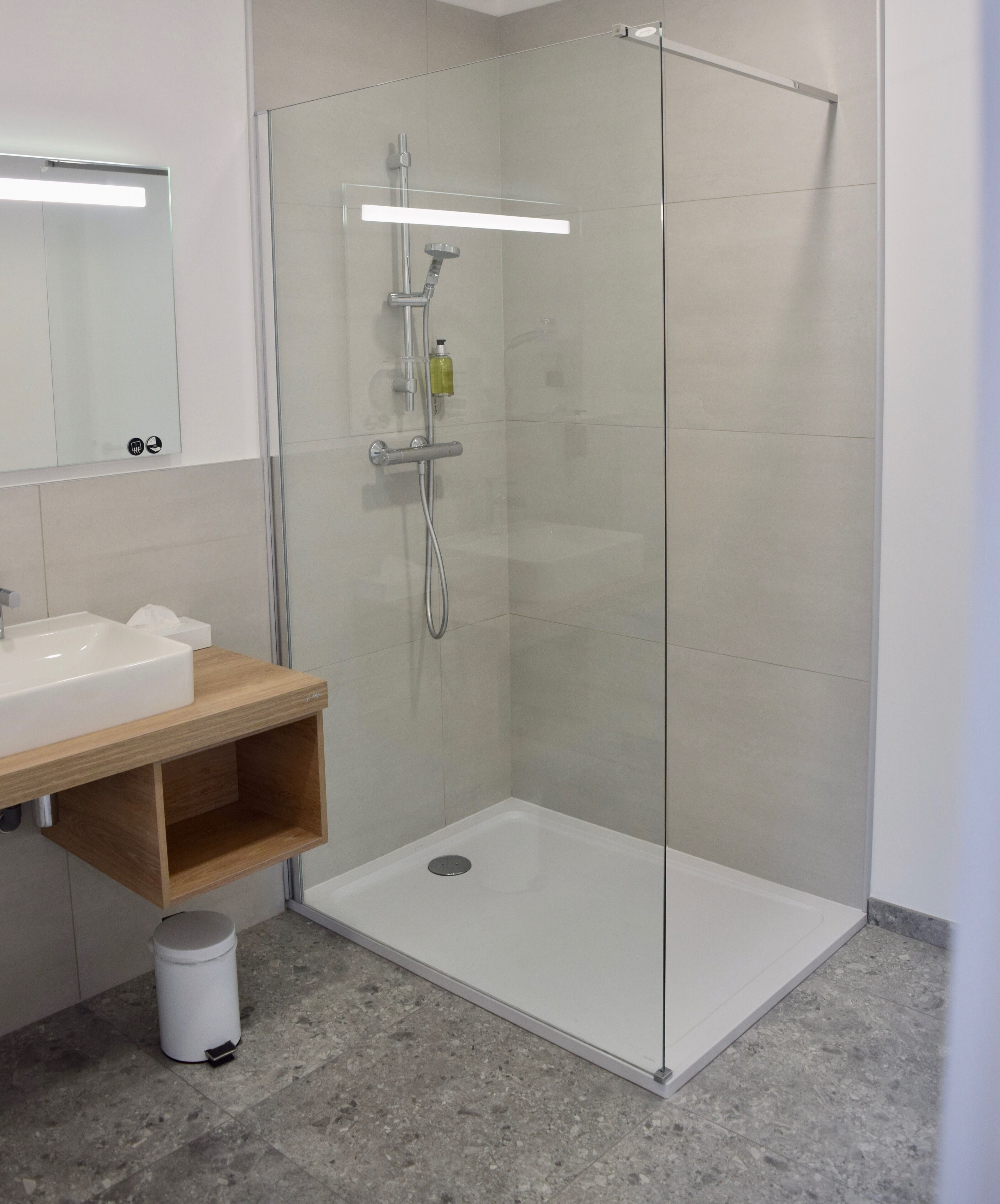 A modern bathroom with a glass-enclosed shower, a wooden vanity, and a white sink.