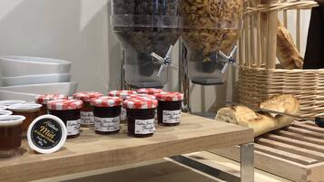 A breakfast buffet with jars of jam, a coffee machine, and bread.
