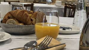 Ein Frühstückstisch mit Croissants, Orangensaft und einer Vase mit einer rosa Blume.