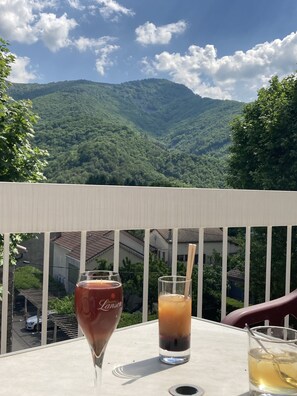 Un balcon avec une table, deux boissons et une vue sur un paysage montagneux.