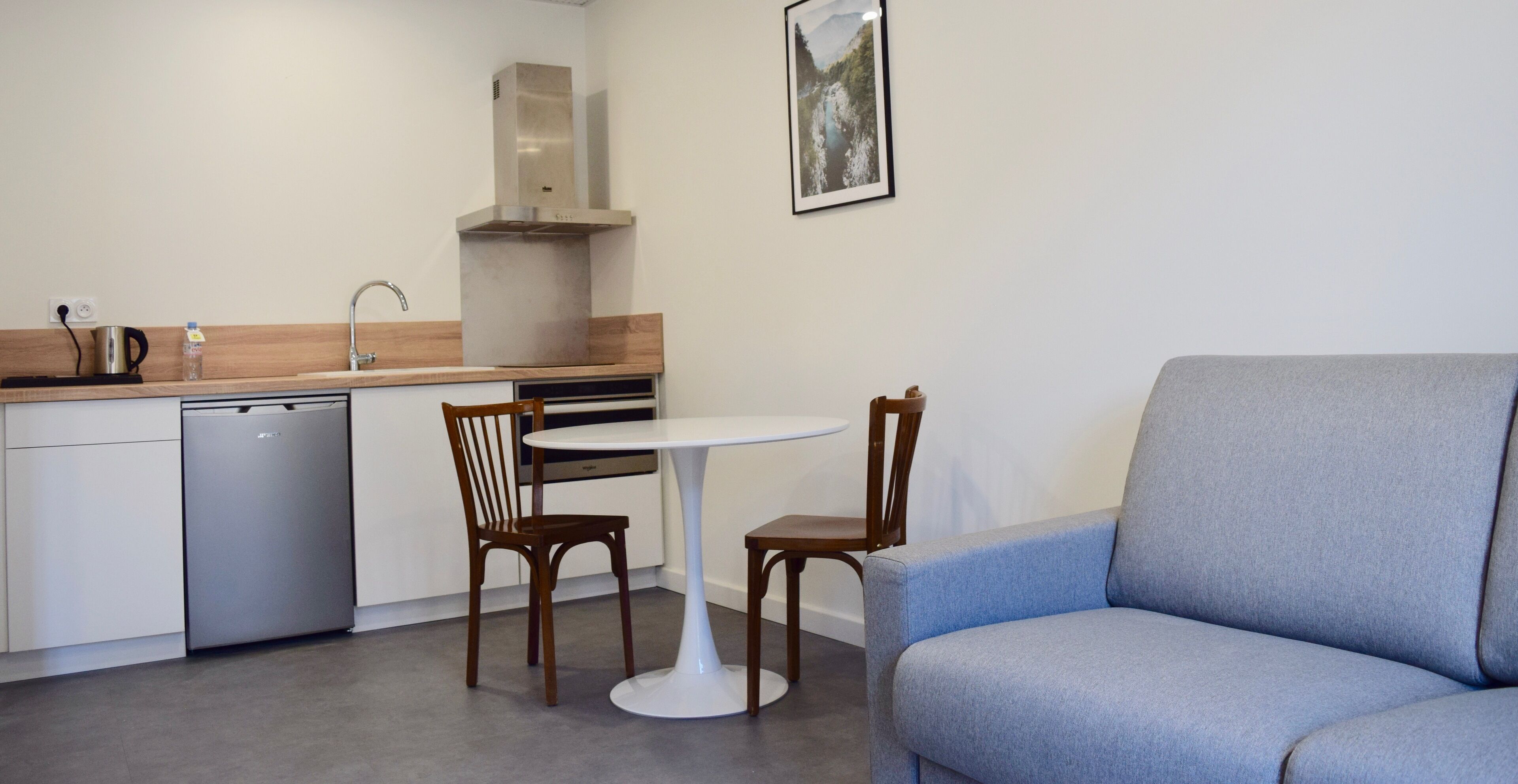Une cuisine compacte équipée d’un lave-vaisselle, d’une cuisinière et d’un coin repas avec deux chaises en bois et une table blanche.