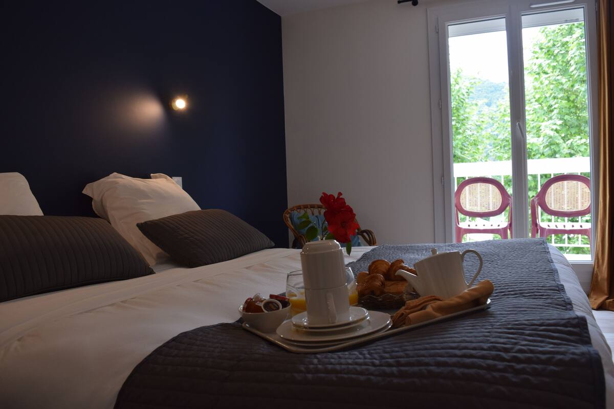 Un lit bien fait, avec des oreillers, un plateau contenant des éléments pour le petit-déjeuner et une vue sur la verdure à l’extérieur.