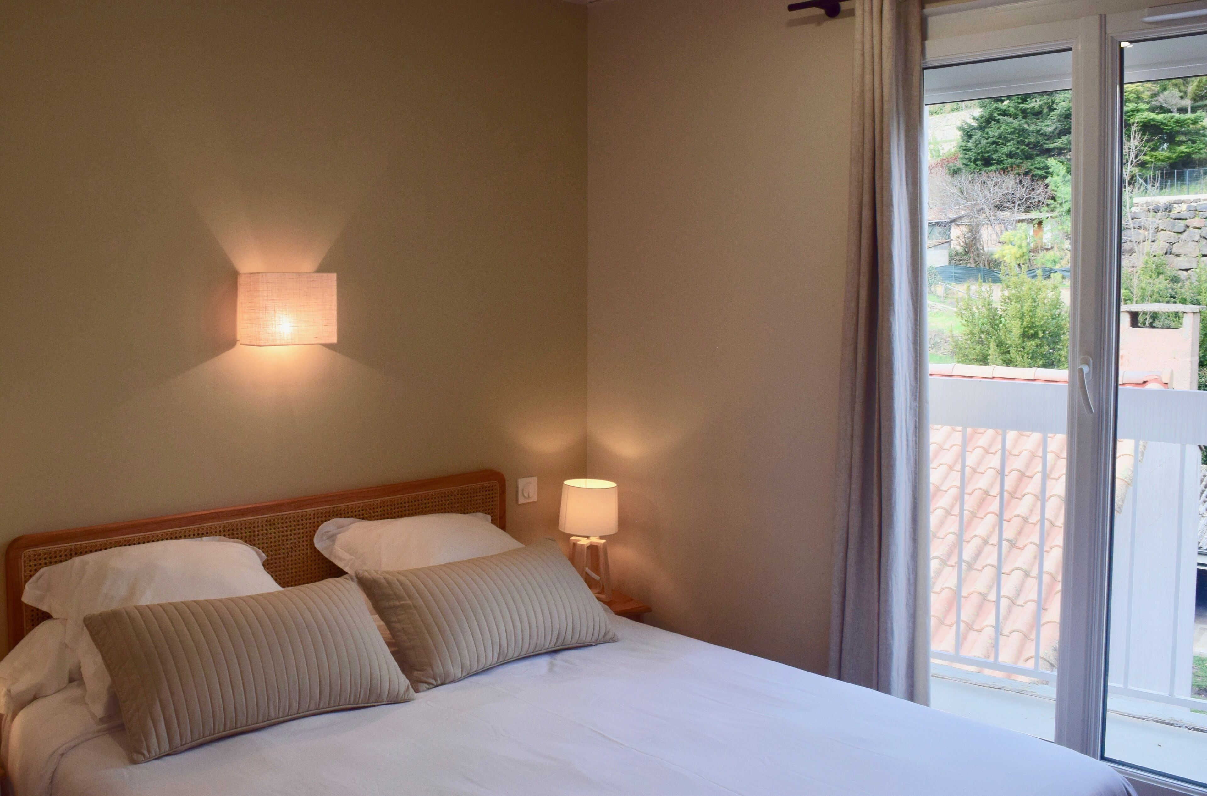 A bedroom with a bed, two bedside lamps, and a view of a garden through a window.