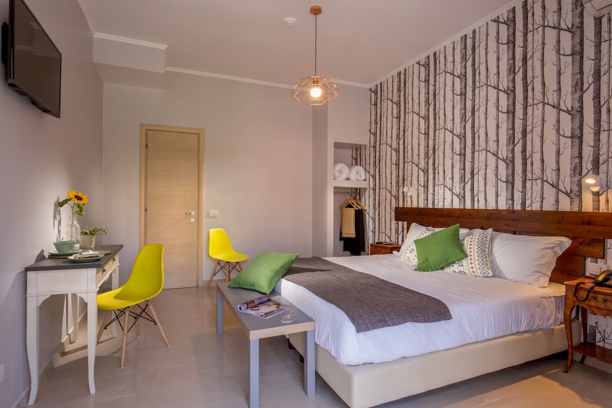 A modern bedroom with a wooden headboard, a large bed, a desk with a chair, and a wardrobe.