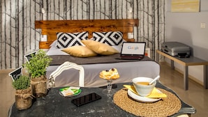 A neatly arranged hotel room with a bed, a laptop, a table with a bowl of soup, a smartphone, and two potted plants. - Urban Garden Hotel (Rome)