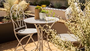 A round metal table with two white metal chairs, surrounded by potted plants and flowers. - Urban Garden Hotel (Rome)