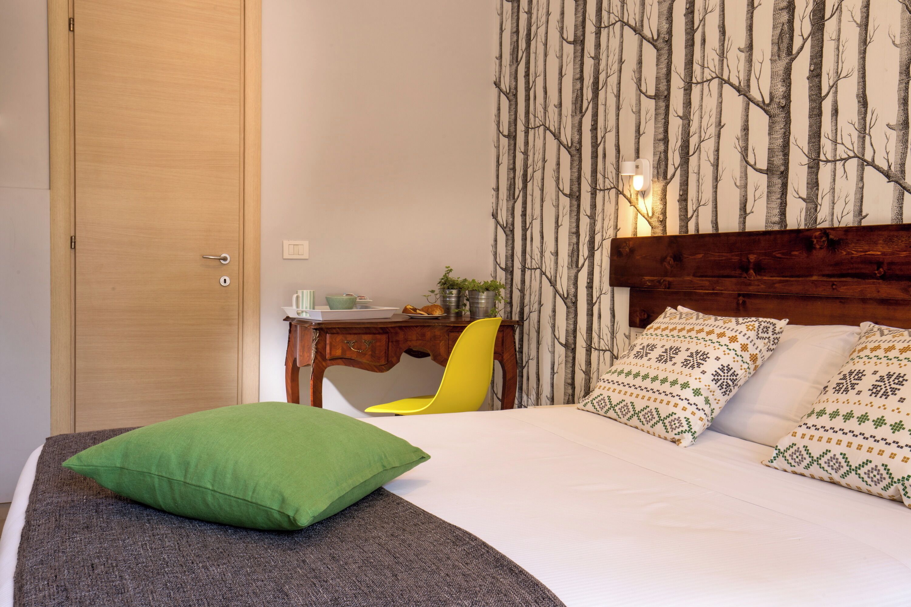 A bedroom with a bed, a desk, a chair, and a wall with a tree pattern.