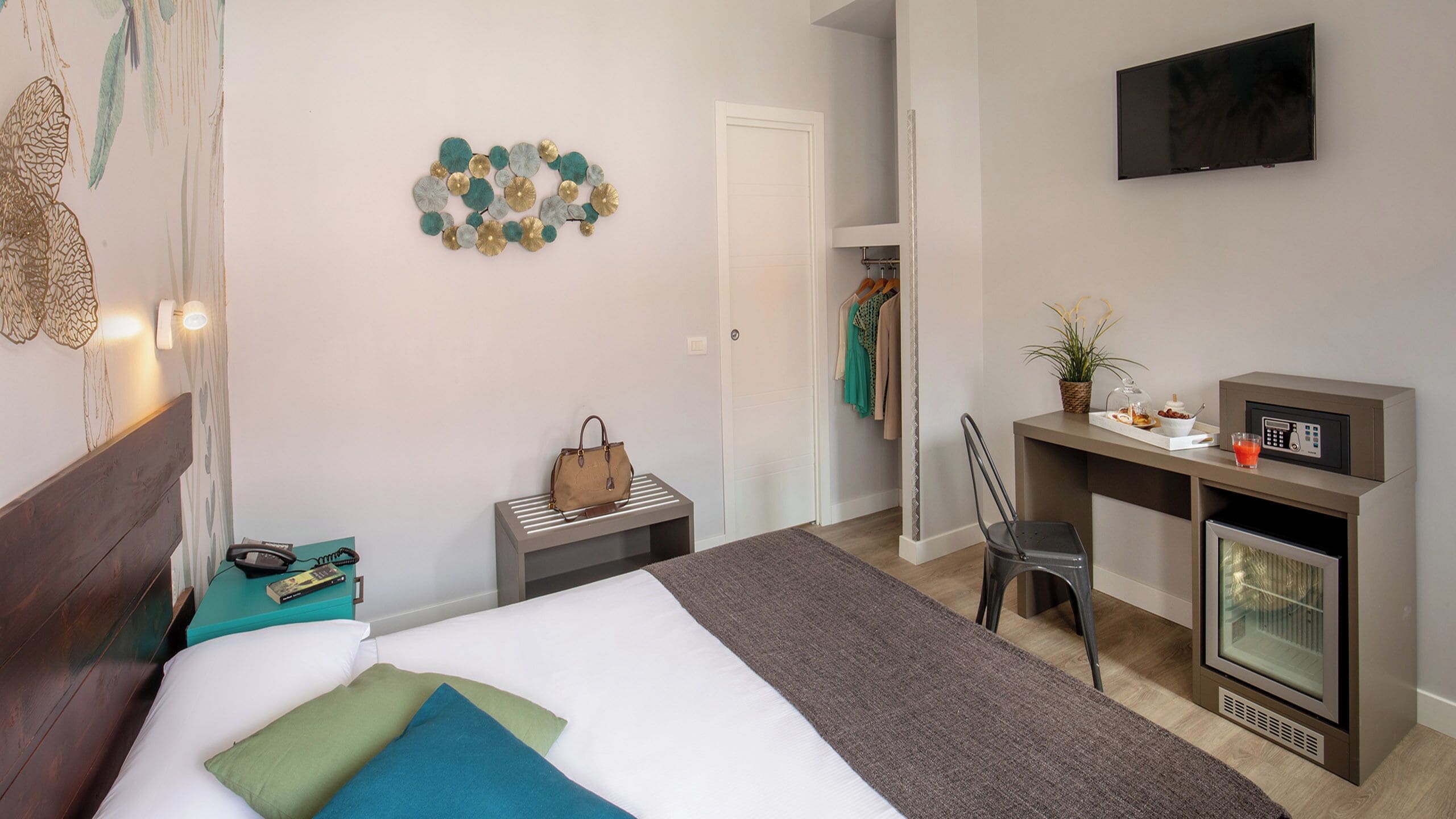 Una habitación de hotel con cama, escritorio, silla, televisor y minibar.