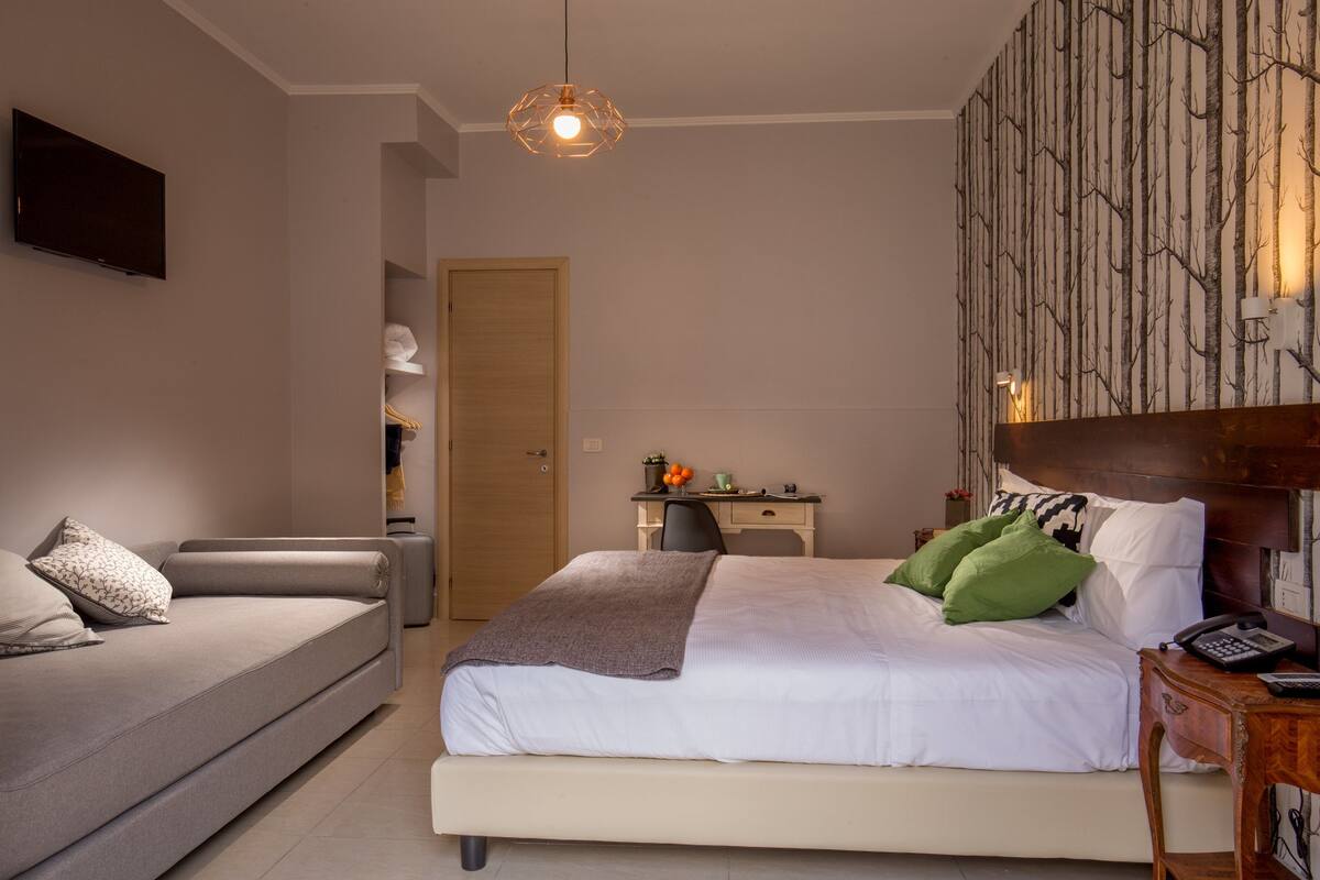 A modern bedroom with a bed, a sofa, a desk, and a wardrobe.